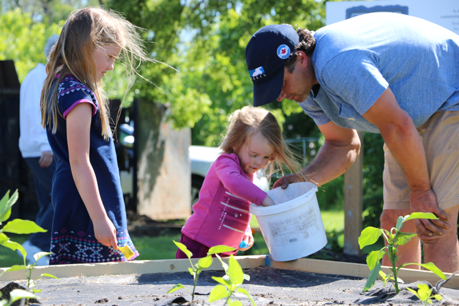 Jordan Elliott of Marine Recycling Corporation shows a youngster how to plant seedlings at the Lockview Park Community Garden in Port Colborne in support of the Port Cares Food Bank.
